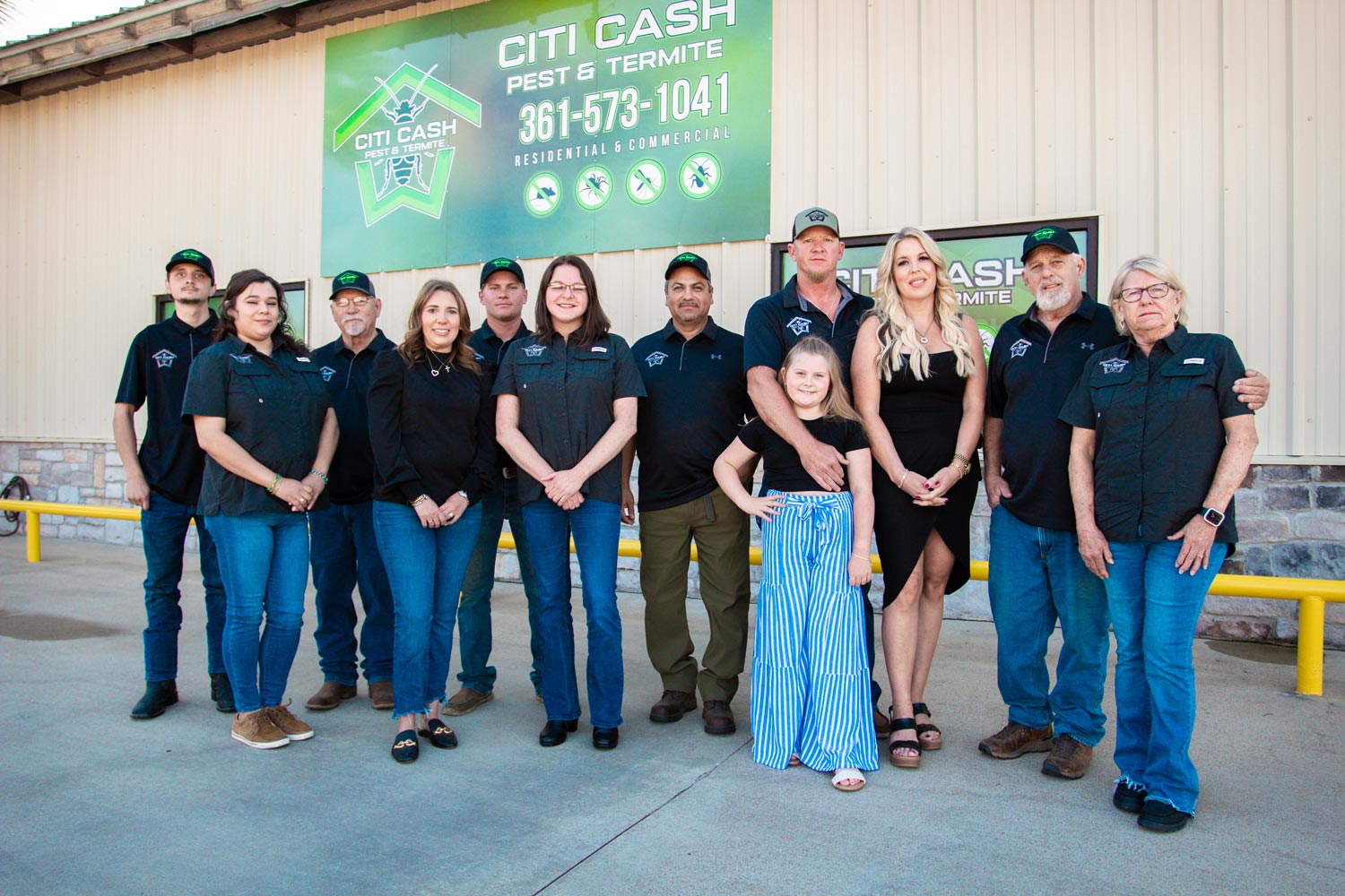 Group of people posing in front of a Citi Cash Pest & Termite business sign, smiling at the camera.