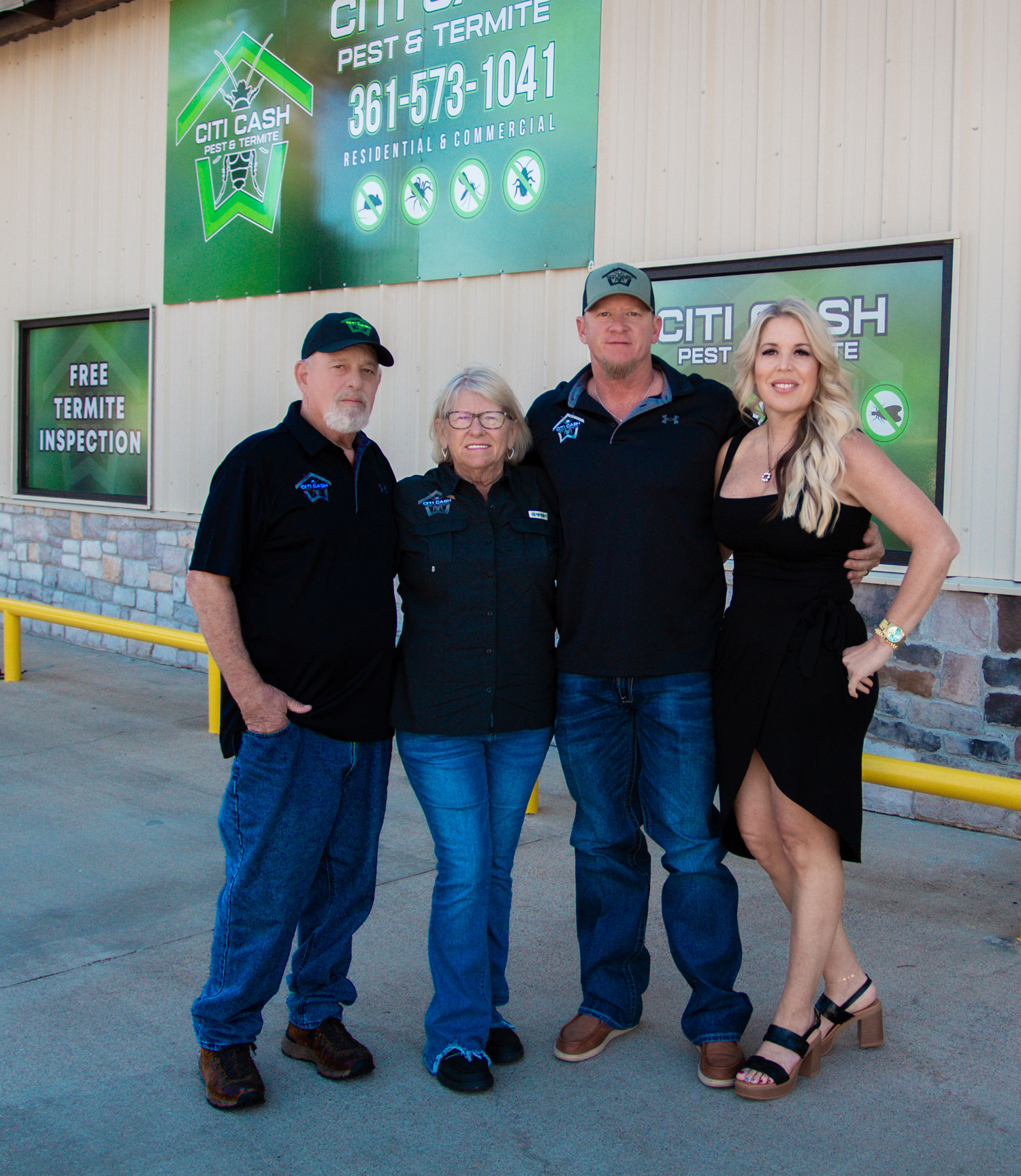 Four people standing together and smiling in front of a pest control business with green signage.