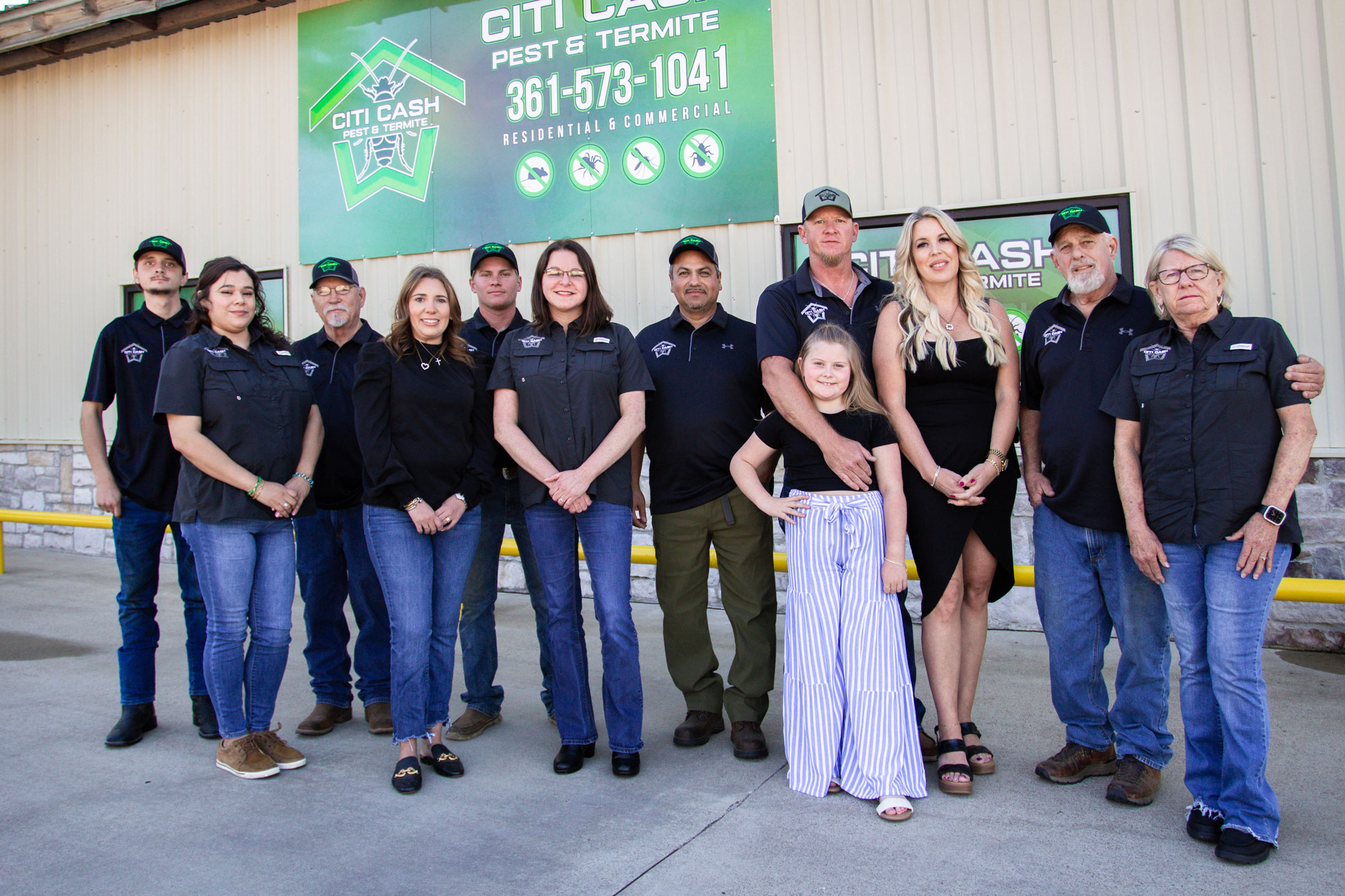 Twelve people of various ages smiling in front of a business sign for Citi Cash Pest & Termite.